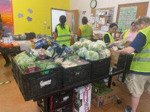 a table of vegetables with a prson in a green vest stancing behind it